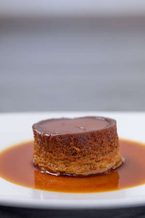 small mexican neapolitan custard with caramel all around on a white plate with an unfocused gray wooden backgroundの写真素材
