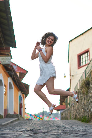 White woman jumping with happiness in the middle of the street on her vacation, with white dress and...