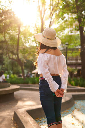 Back view of young woman wearing white shirt and hat in the park