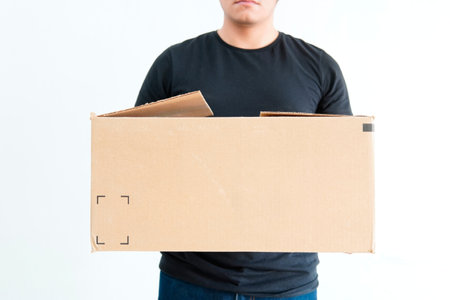 Young latin guy delivering packages, holding a cardboard box, wearing black t-shirt and jeans, not recognizable person, white background.の写真素材