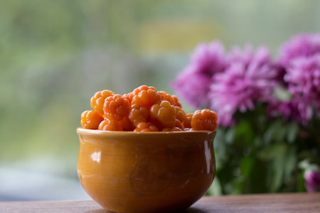 Rubus chamaemorus. Cloudberry close up in orange bowl on wooden table,autumn harvest in norwegian...