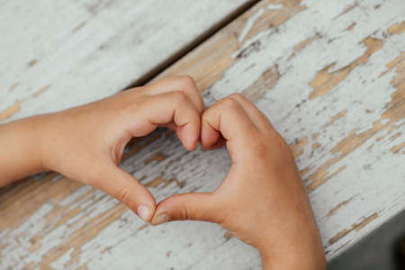 On a wooden background, a child's hands show a heart.の写真素材