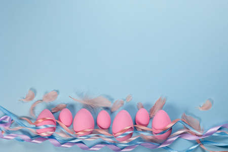 Pink Easter eggs on a blue background with ribbons and feathers with a place for text