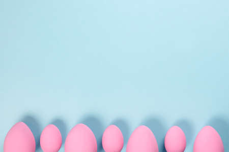 Pink Easter eggs on a blue background with ribbons and feathers with a place for text