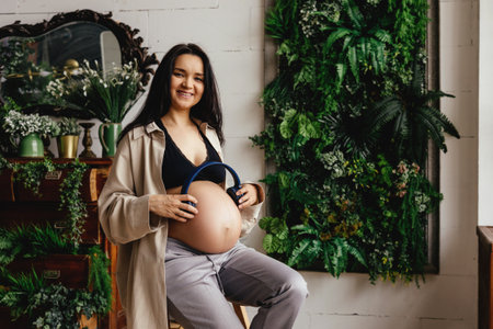 A beautiful pregnant girl strokes her stomach in a home interior.の写真素材