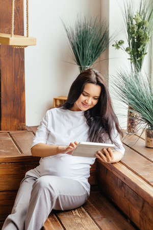 Lovely pregnant girl is holding a tablet.の写真素材