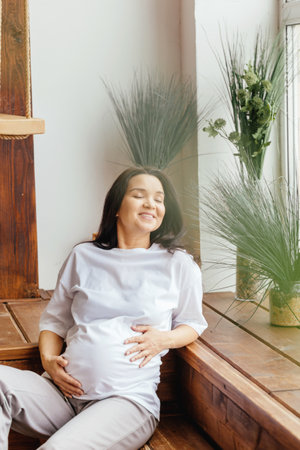 A beautiful pregnant girl strokes her stomach in a home interior.