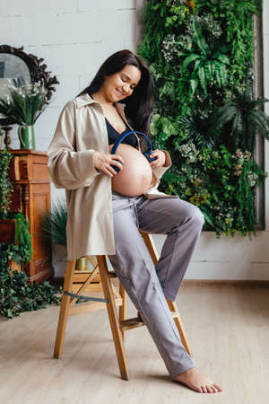 A beautiful pregnant girl strokes her stomach in a home interior.
