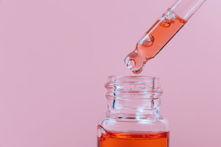 Pipette with a glass bottle on a pink background and with oil.