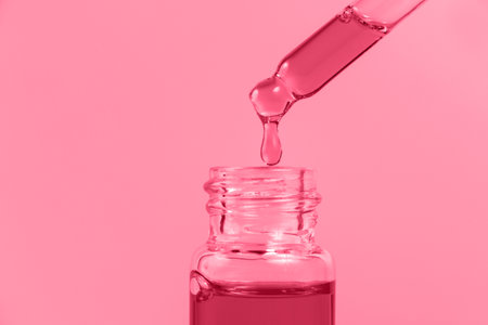 Pipette with a glass bottle on amagenta background and with oil. trendy color 2023.の写真素材