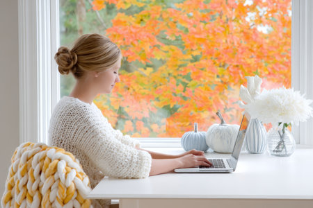 Young caucasian female working on laptop in cozy room with autumn pumpkin decor.の素材