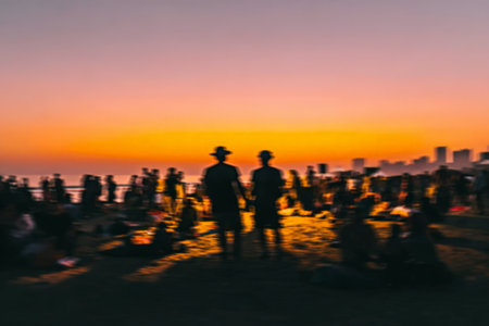 Silhouetted crowd watching sunset by the beach in vibrant urban setting.の素材