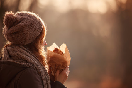Young caucasian woman enjoying warm pastry outdoors in winter attire.の素材