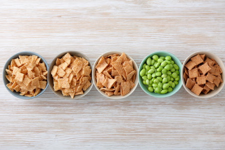 Variety of crunchy snacks and edamame in bowls on wooden table.の素材