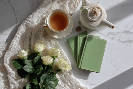 Elegant tea setting with roses and books on marble table.の素材