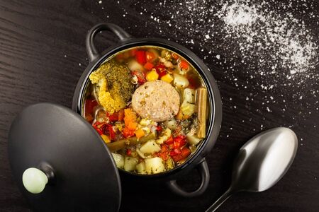 vegetable soup with meatballs in a dark tureen with a lid on a black table with scattered salt