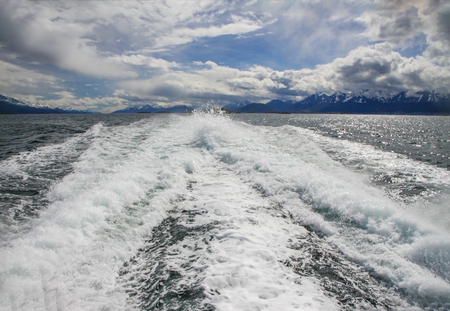 Foaming trail on water surface behind speed boat on natural background with dramatic sky and snow-covered mountains. Argentina, Beagle Channelの写真素材