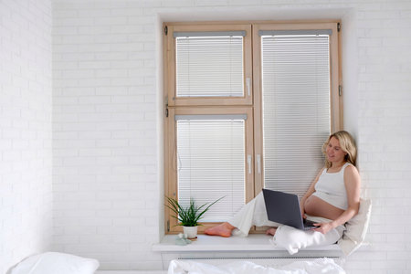A young pregnant woman is working on a laptop. Pregnant freelancer. Portrait young pregnancy woman using online laptopの写真素材