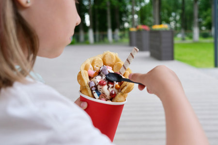 Hong Kong or bubble waffles with ice cream, chocolate tubes and marmalade in the hands of a childの写真素材