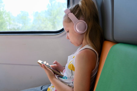 A schoolgirl girl rides a train, listens to music with headphones and uses a smartphone. Traveling...