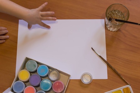 White sheet mock up with brushes, acrylic paints and child grasping handの写真素材