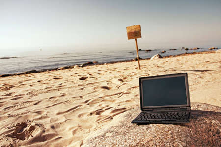 Single black laptop and woodens sin in background alone at beach.の写真素材