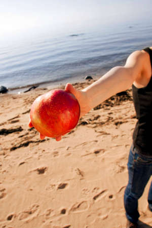 Hand of young woman offering red apple at beach.の写真素材