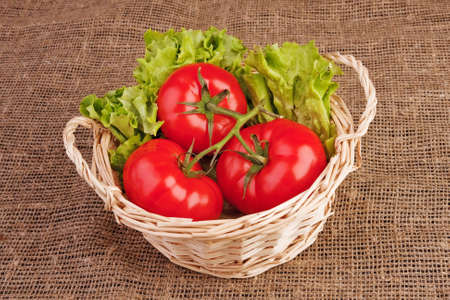 Bunch of three red tomatoes and lettuce in basket on rough linen fabric.の写真素材
