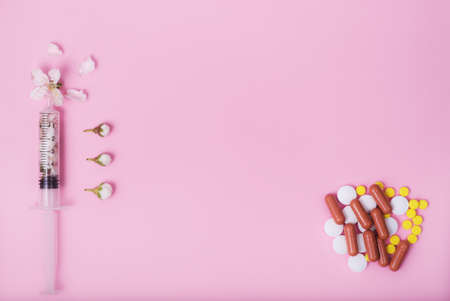 Many different tablets and capsules and a syringe filled with small white flowers on a pink monotone background. Place text. Copyspace. Banner. Symbol. Allergy Medicineの写真素材