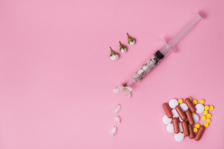 Many different tablets and capsules and a syringe filled with small white flowers on a pink monotone background. Place text. Copyspace. Banner. Symbol. Allergy Medicineの写真素材