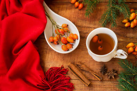 winter, warm atmosphere. A cup of hot black tea with a red scarf, rose berries and spruce on a wooden background Winter cozy evening. Flat lay, layout, place for text, post card, high resolutionの写真素材
