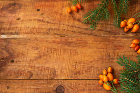 Winter, warm atmosphere. Frame with red scarf, rose berries and spruce on wooden background. Winter evening. Flat lay, layout, place for text, post card, high resolutionの写真素材