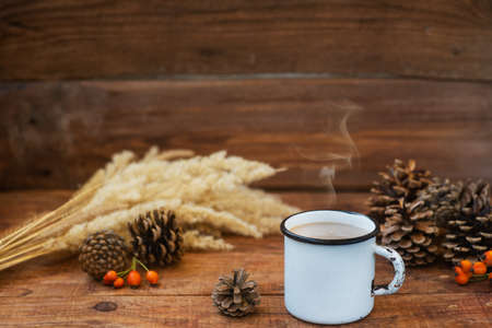 Christmas background in rustic style. A metal mug with hot milk tea stands on a tablecloth, on a wooden surface among pine cones, spruce branches, spikelets of wheat and rosehips. Copy Space, Flat layの写真素材