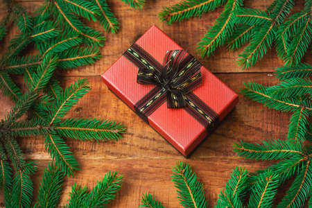 Christmas background. Spruce branches in the form of a round frame and a gift in the middle on a wooden background. Top view. Christmas or New Years card. Flat lay, layout