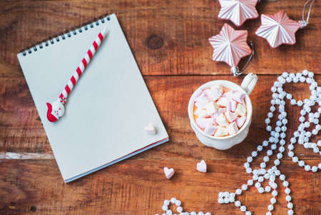 Christmas background. Notebook, Christmas balls, cup with coffee with marshmallows on a wooden background. Copy space Top view. Christmas or New Years card. flat layの写真素材