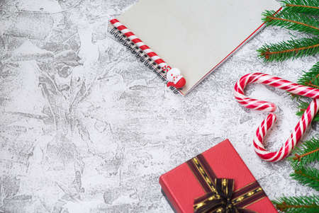 New Year's or Christmas composition of spruce green branches, New Year's gift, notebook, cookies and Christmas lollipops on a bright textural background. Flat lay, layout, copy spaceの写真素材