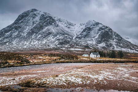 Dramatic winter landscape of Glen Coe with the iconic white cottage at the foot of Buachaille Etive Mor, River Coupall and stormy clouds on the horizon.の写真素材