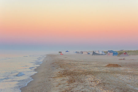 the sea with fog at sunrise and tents on the beachの写真素材
