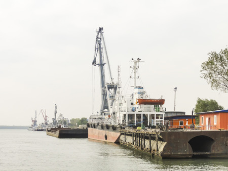 Shipyard with various stationed vessels and industrial cranes along the riverの写真素材