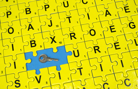 Connected yellow puzzle pieces with letters , two of them missing and a key , on blue backgroundの写真素材