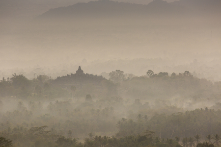 Colorful sunrise over Merapi volcano and Borobudur temple in misty jungle forest, Indoneisaの写真素材