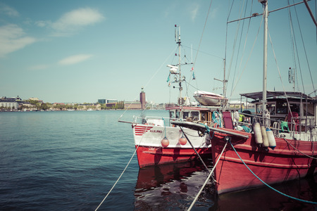 Old city buildings and old boats on water under blue sky in Stockholm, Sweden.のeditorial素材
