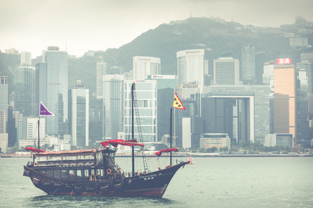 HONG KONG, JUNE 05, 2018 : Traditional Chinese wooden sailing ship with red sails in Victoria harbor. Skyscrapers in downtown of Hong Kong are visible from Kowloon side.のeditorial素材