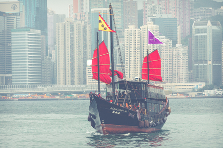 HONG KONG, JUNE 05, 2018 : Traditional Chinese wooden sailing ship with red sails in Victoria harbor. Skyscrapers in downtown of Hong Kong are visible from Kowloon side.のeditorial素材