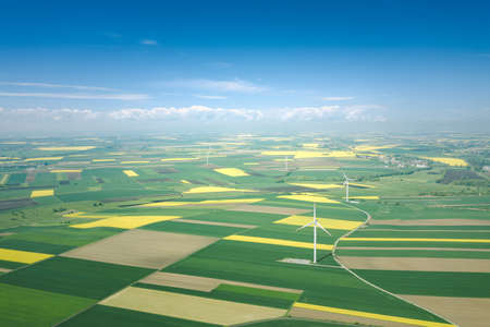Aerial view of wind turbine. Rapeseed blooming. Windmills and yellow fields from above. Agricultural fields on a summer day. Renewable Energy.の写真素材