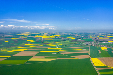 Aerial view of wind turbine. Rapeseed blooming. Windmills and yellow fields from above. Agricultural fields on a summer day. Renewable Energy.のeditorial素材