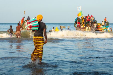 TANJI, THE GAMBIA - NOVEMBER 21, 2019: Scene with men and women carrying fish from the boats to the...