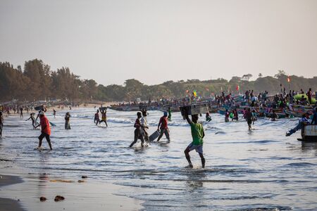 TANJI, THE GAMBIA - NOVEMBER 21, 2019: Scene with men and women carrying fish from the boats to the beach on Tanji, Gambia, West Africa.のeditorial素材