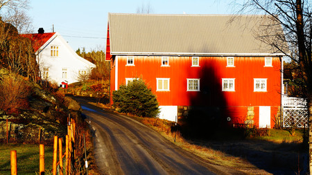 Elevation big red wooden building, barn to store hay and farm tools. North Sea Coast. Norwegian winter. The sun low on the horizon. Telemark region of Norwayの写真素材
