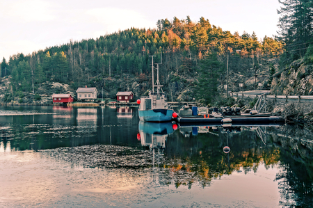 Floating dock, a small fishing boat moored. Sunset over frozen lake in the region of the North Sea coast. Around the rocks overgrown with trees. HDR view. Norwegian winter. Telemark region of Ostlandet. Eastern Norway.の写真素材